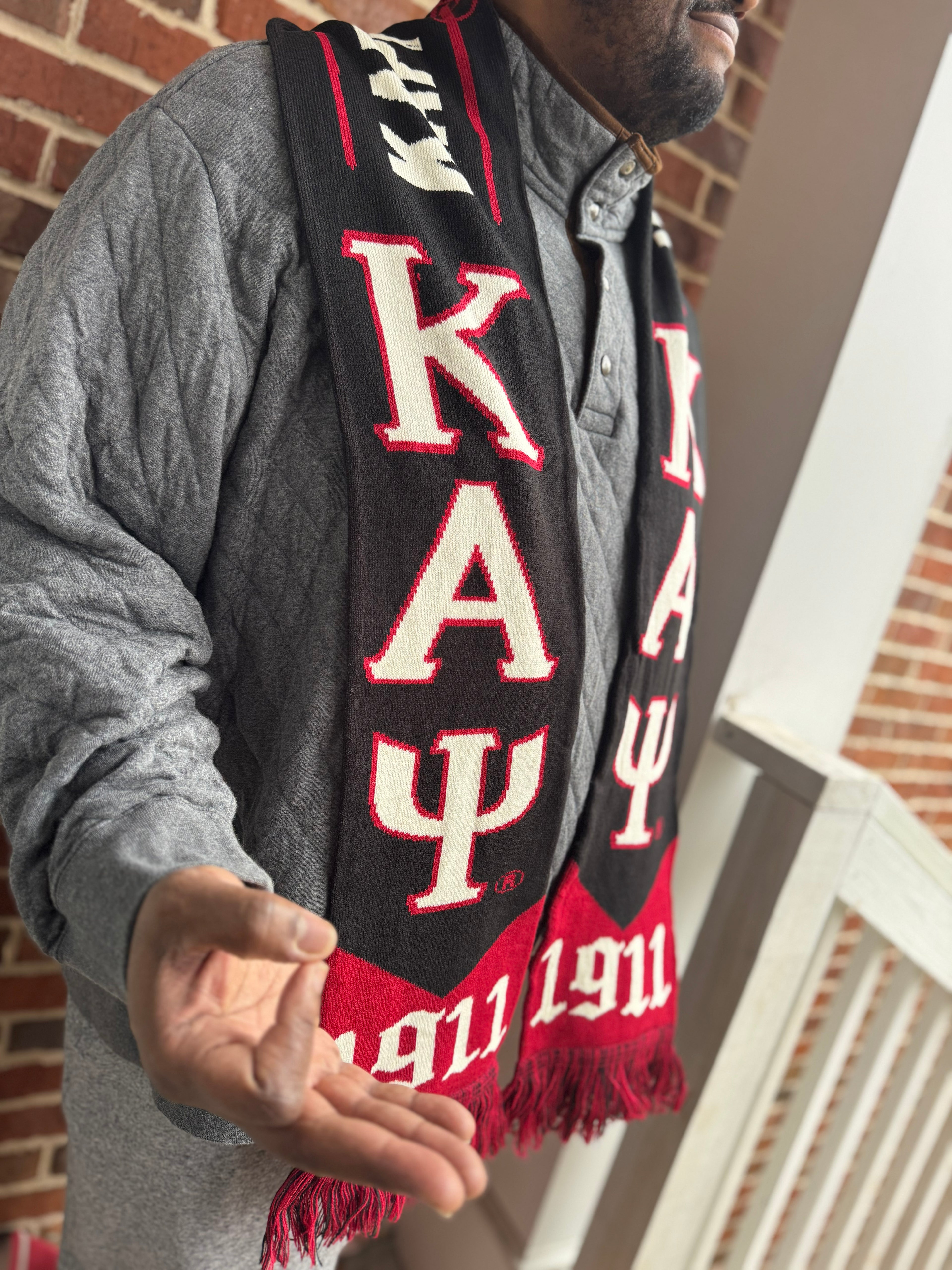 Person wearing a black and red scarf with Greek letters and numbers, standing indoors.